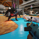 A Brute charges a prone player while two other characters point their weapon at it in a retrofuturist room.